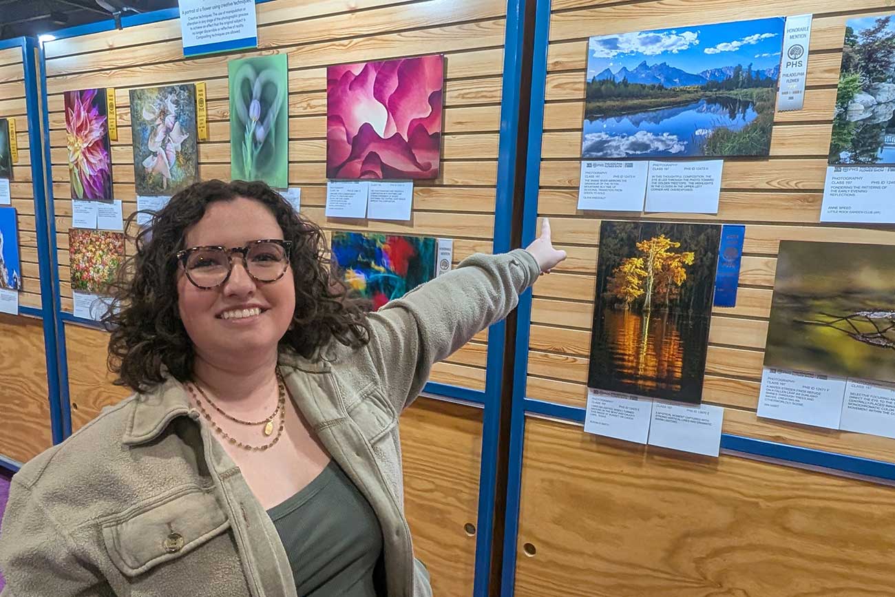 Olivia pointing at her ribbon winning photography at the PHS Flower Show 2025