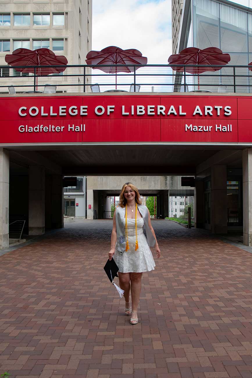 Rose walking towards the camera wearing her Temple University graduation regalia